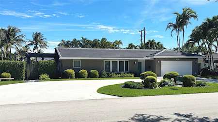Single-story gray home with an attached garage, broad driveway, and palm-lined landscaping.