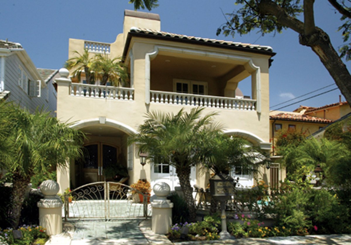Cream Mediterranean-style home with a covered balcony, arched entrance, and landscaped gated frontage.