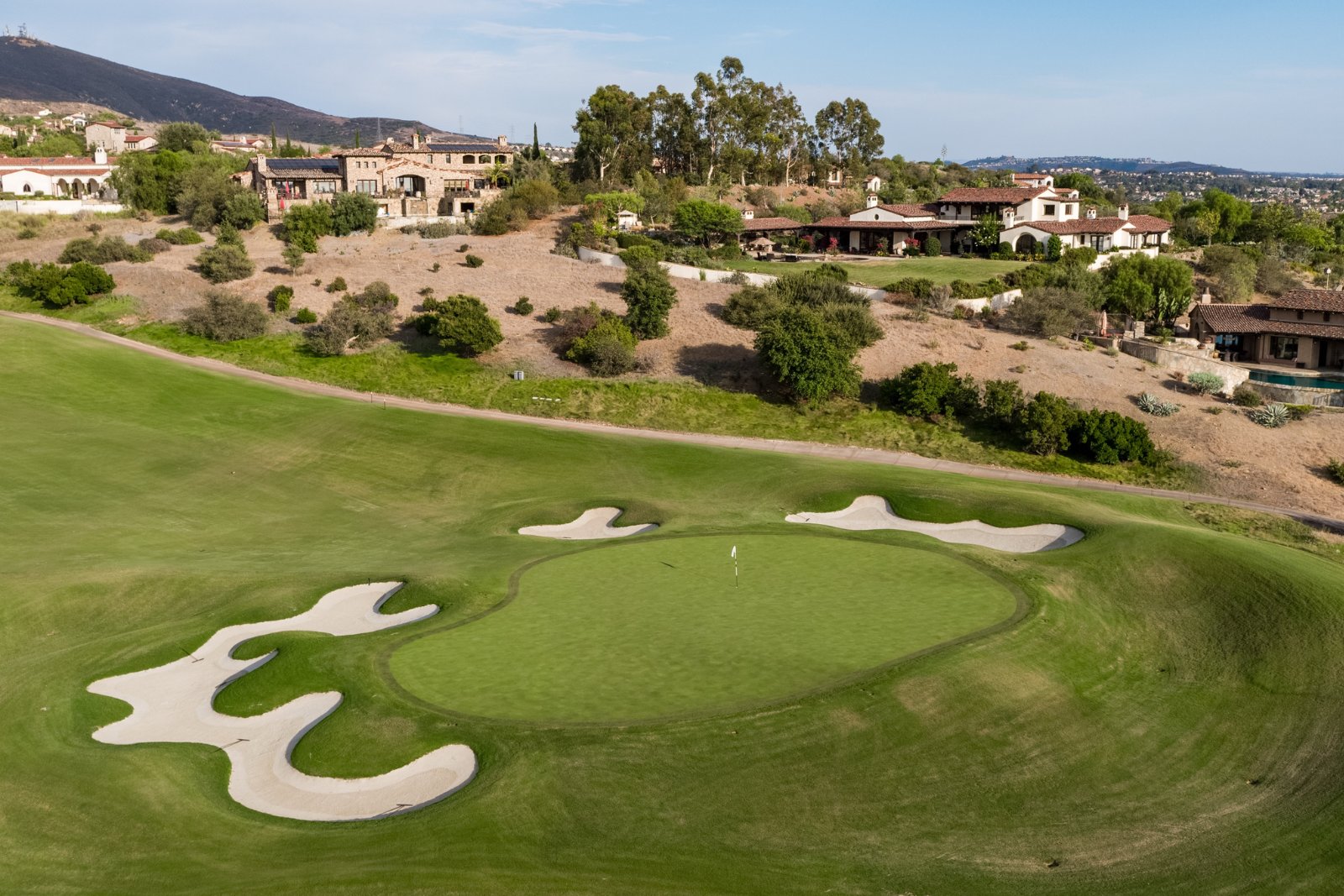 Golf green and bunkers on the Santaluz golf course with homes on the hillside