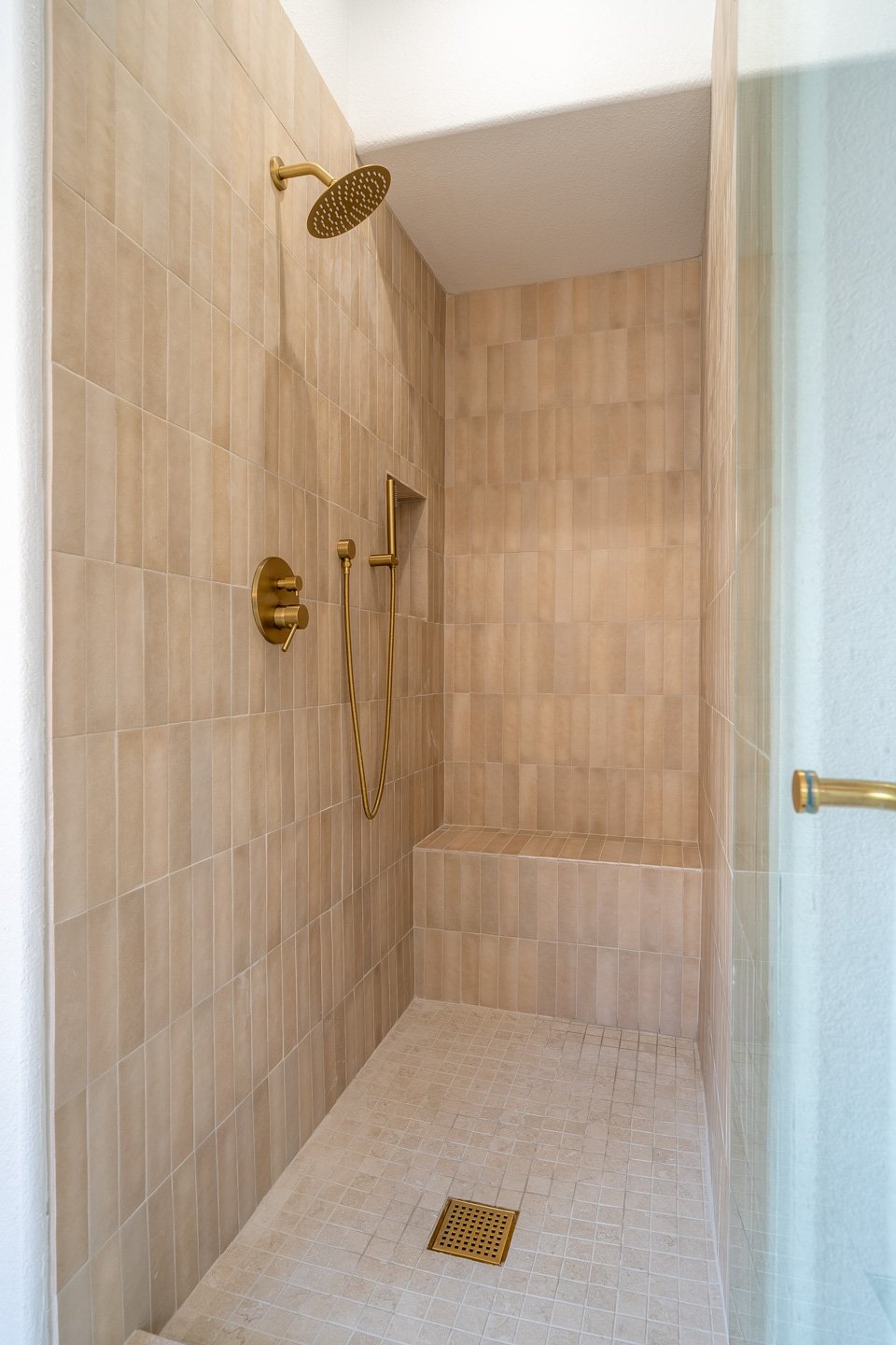 Beige tiled walk-in shower with brass fixtures, a built-in bench, and glass enclosure.