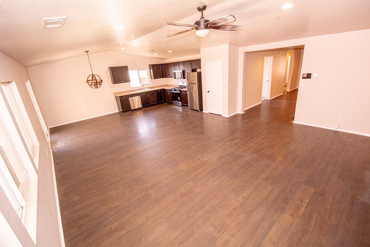 Open living area with dark-cabinet kitchen, stainless steel appliances, and brown wood-look flooring.