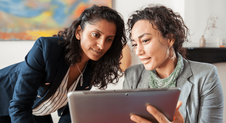 Two women in professional attire examining a tablet together, engaged in a discussion or collaboration.