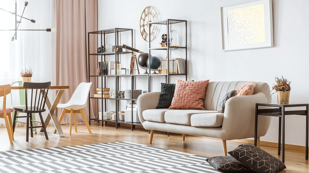 Bright living room with a cream sofa, open shelving, dining area, and geometric rug.