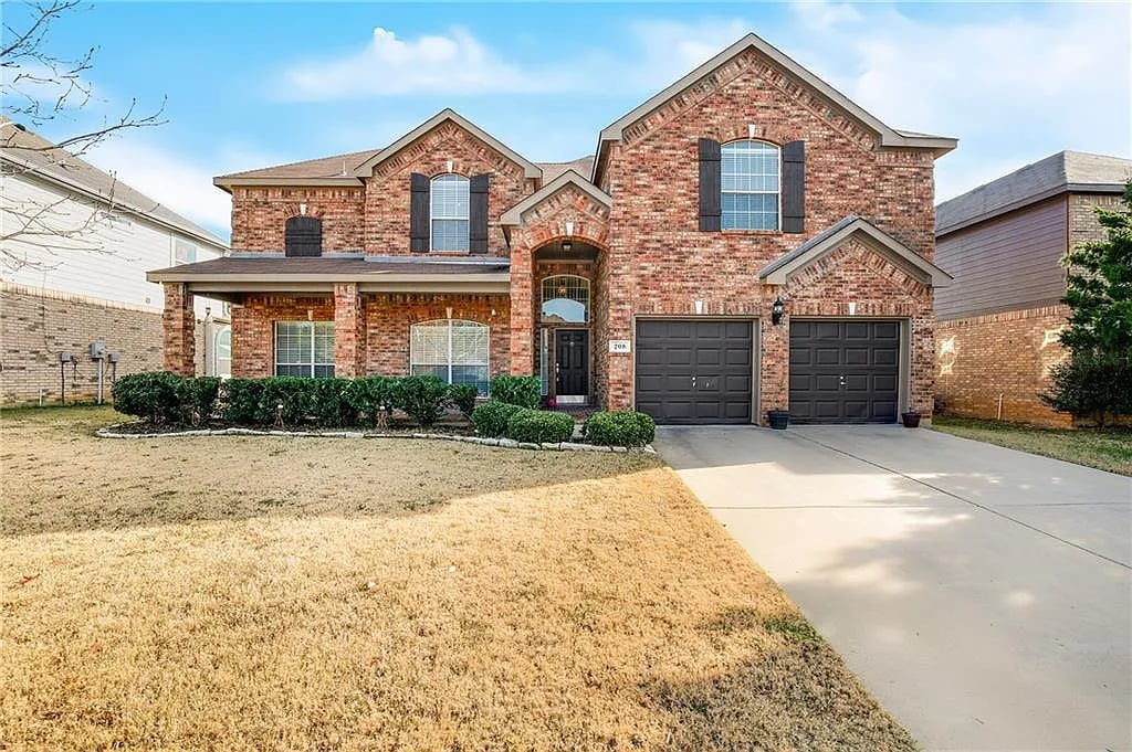 Two-story brick house with two garage doors, a wide driveway, and a dormant front lawn.