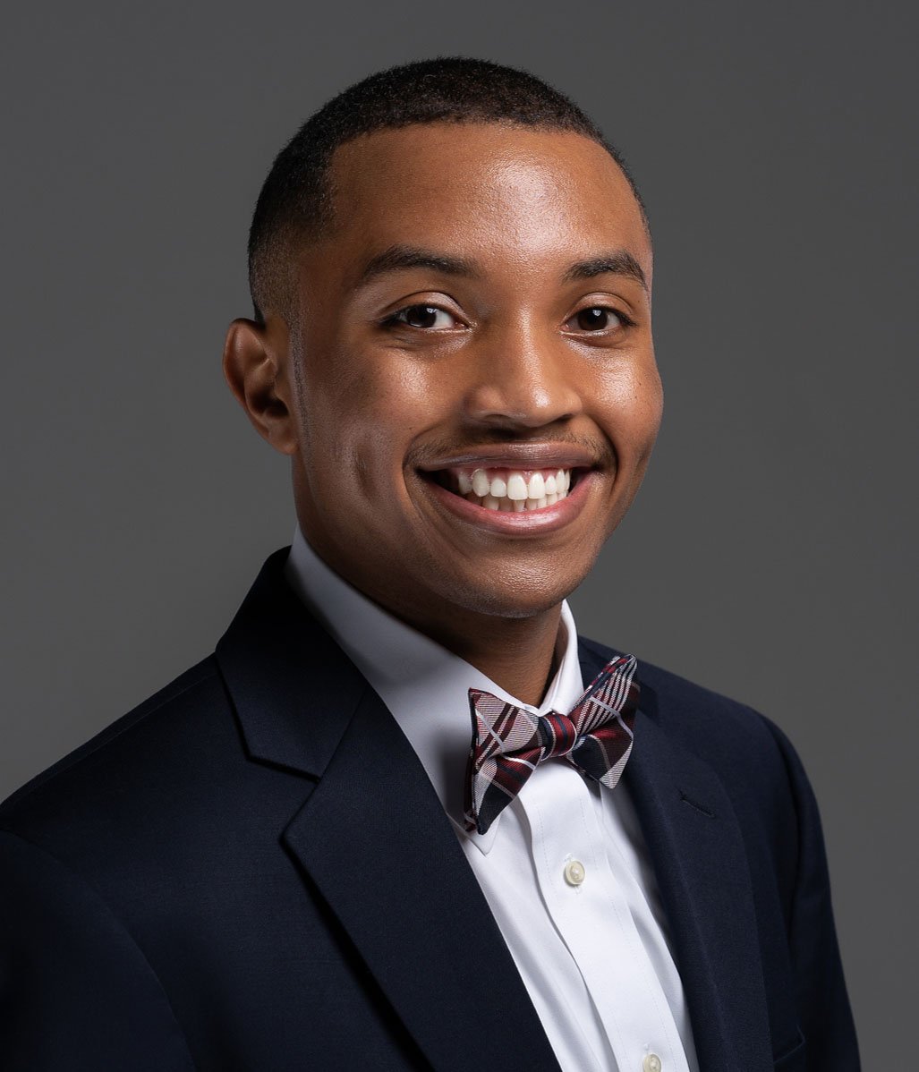 Trent Dodson smiling in a dark suit and plaid bow tie.