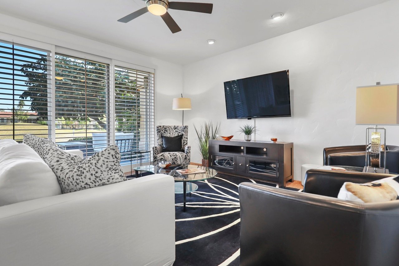 Furnished living room with wide windows, dark leather chairs, and a wall-mounted television.