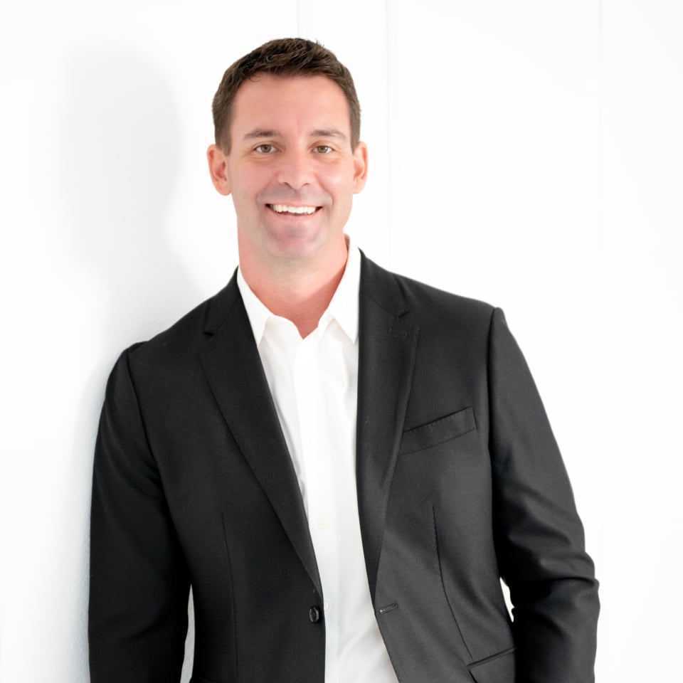 Smiling man in a black suit jacket and white shirt against a white background.