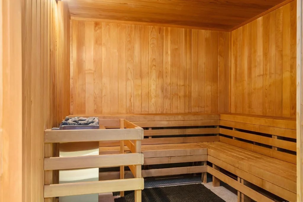 An interior view of a wooden sauna room with benches and a heater with hot stones, an amenity at the Madrone.