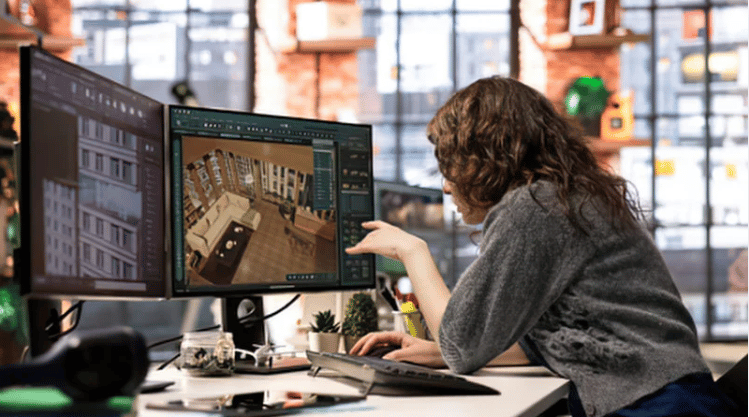Woman points to a floor plan on a monitor at her desk.