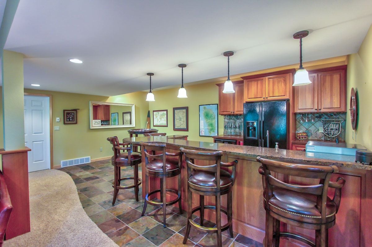 Kitchen with a long granite island, bar stools, and reddish wood cabinetry.