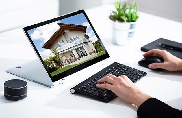 Hands use a laptop to view a modern two-story house.