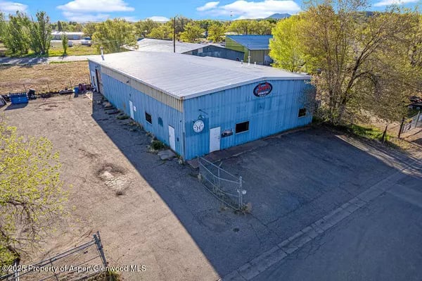 Blue metal commercial building with a fenced paved lot and trees.