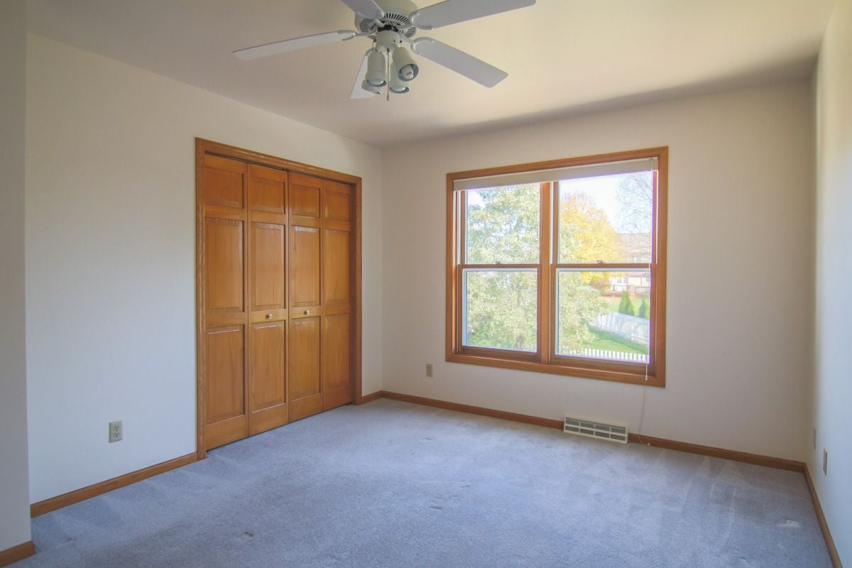 Vacant bedroom with built-in wooden closets, a ceiling fan, and a large window.