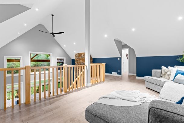 Loft living area with vaulted ceiling, wooden railing, and gray sectional beside a dark blue wall.