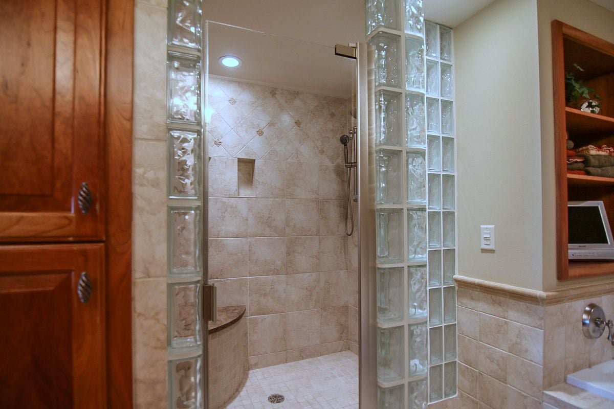 Bathroom with a tiled walk-in shower, glass-block walls, and warm wood cabinetry.