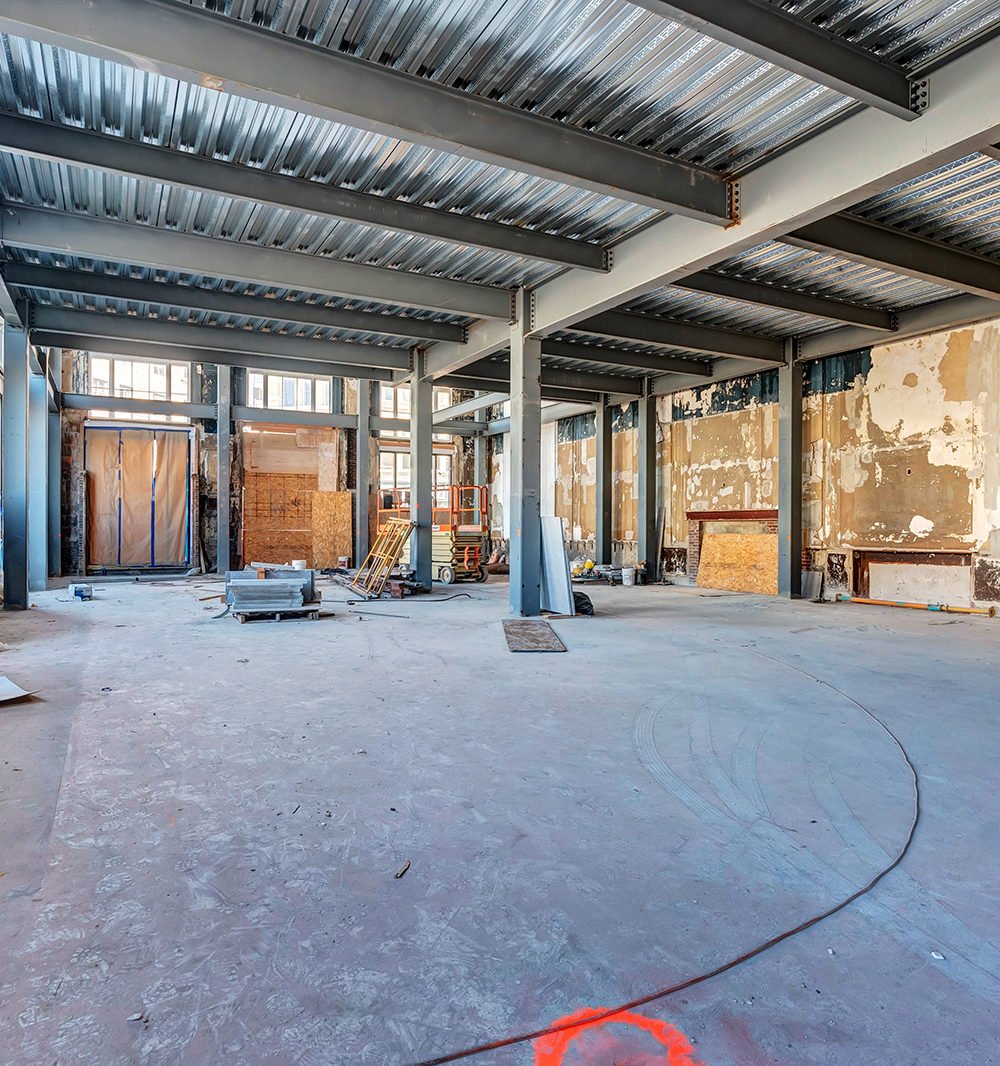 Unfinished interior with exposed steel beams, stripped walls, and construction materials.
