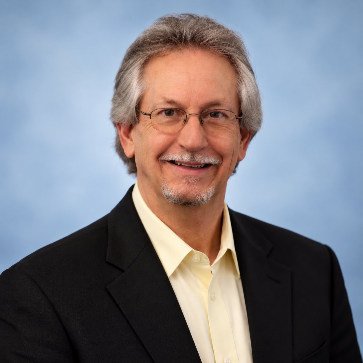 Richard Rixey smiling in glasses and a black jacket against a blue background.