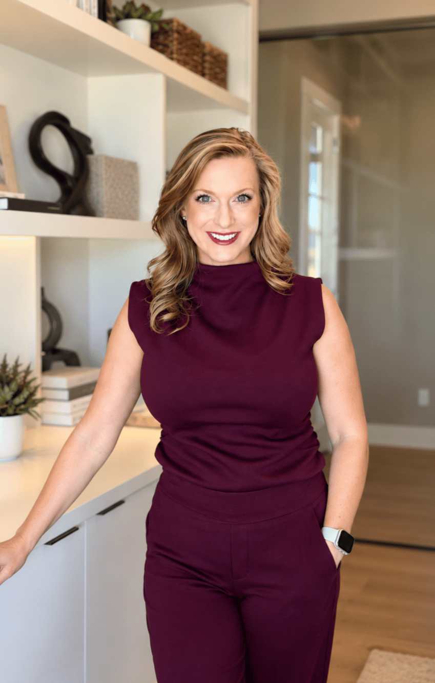 Smiling woman in a burgundy outfit standing beside a kitchen counter and built-in shelves.