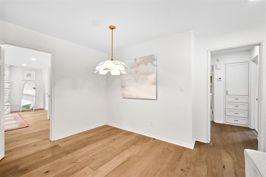 Dining area with wide-plank oak floors, a white pendant light, and abstract art.