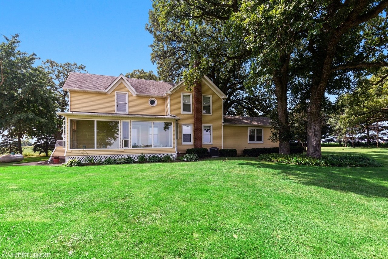 Yellow two-story home with a glass-enclosed porch, brick chimney, and spacious shaded lawn.