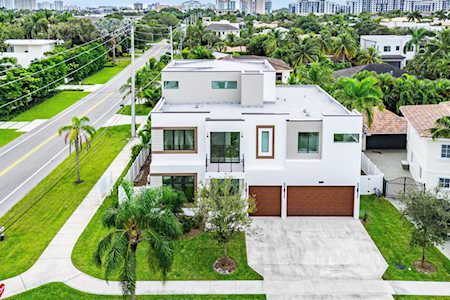 Modern white home with a flat roof and double garage, surrounded by tropical landscaping.