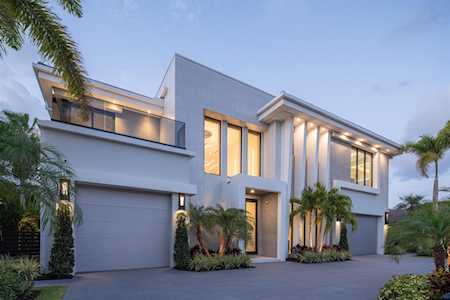 Modern two-story home with a white facade, illuminated windows, and tropical landscaping.