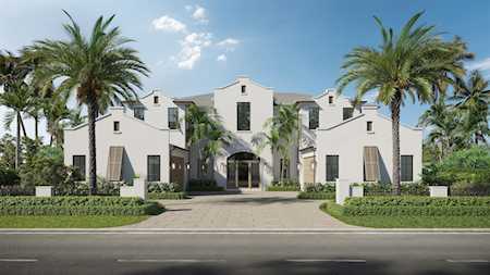 White stucco building with a central arched entrance, palm trees, and a landscaped driveway.