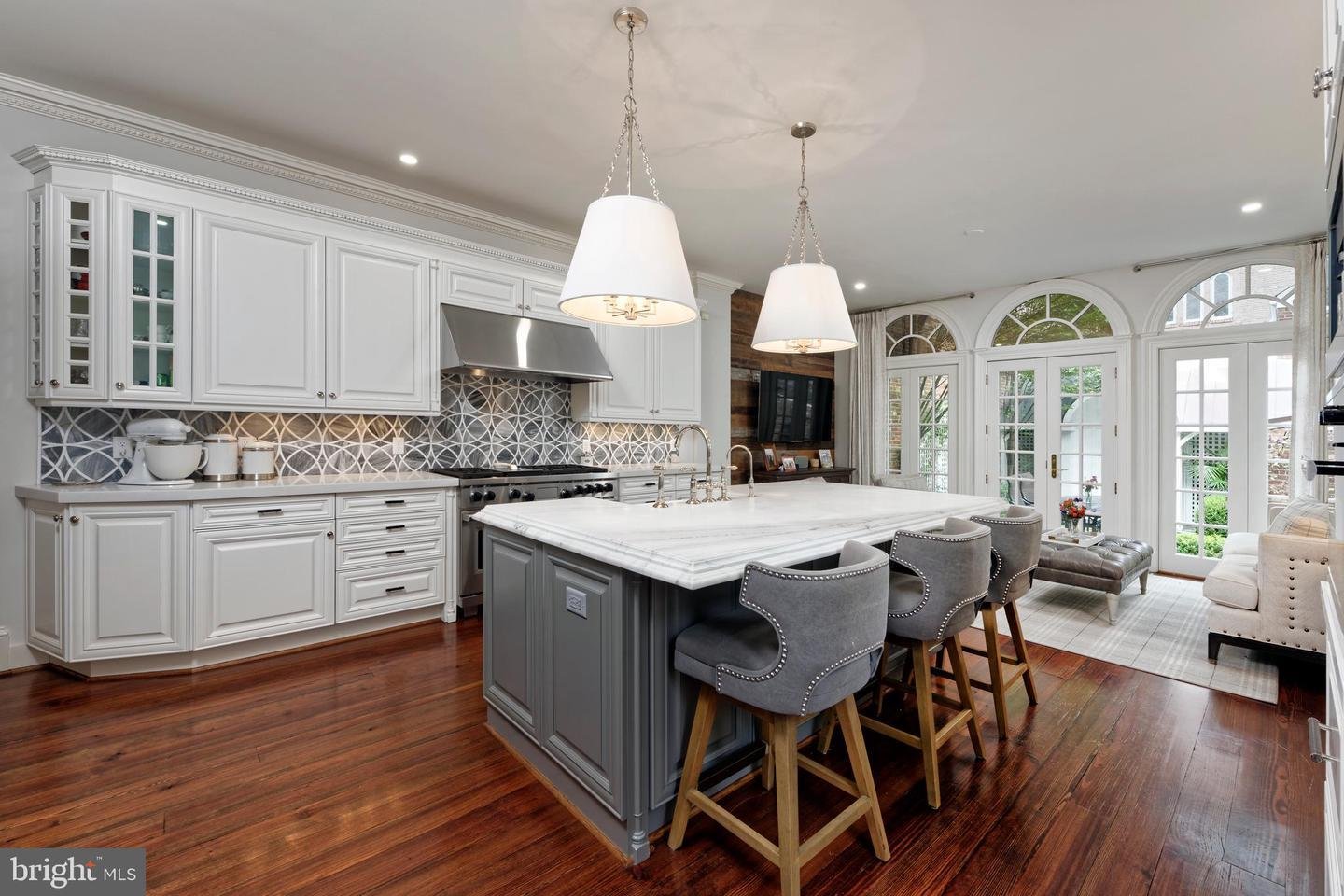 Kitchen with a large gray island, white cabinetry, patterned backsplash, and arched garden-facing windows.