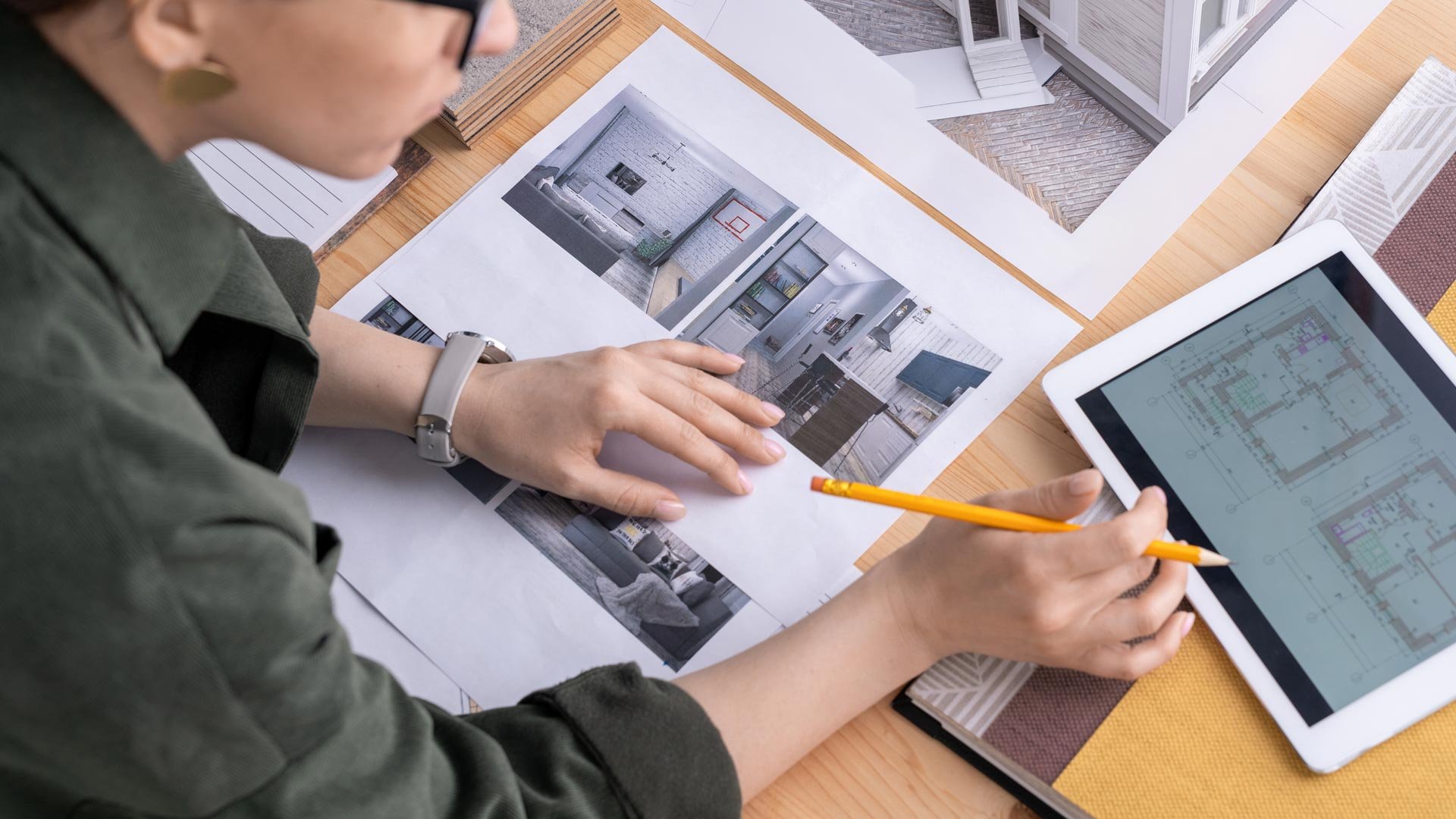 An overhead view of a real estate marketing specialist evaluating professional interior photographs and cross-referencing a digital floor plan on a tablet to select the highest impact assets for a property listing, illustrating the strategic campaign curation required when determining how to sell your house GTA for top dollar