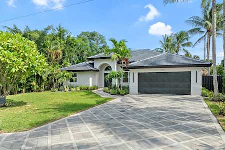 Single-story home with a dark double garage, wide paver driveway, and tropical landscaping.