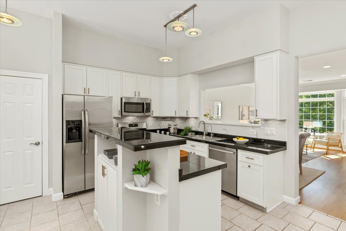 Bright white kitchen with dark countertops, a central peninsula, and stainless steel appliances.