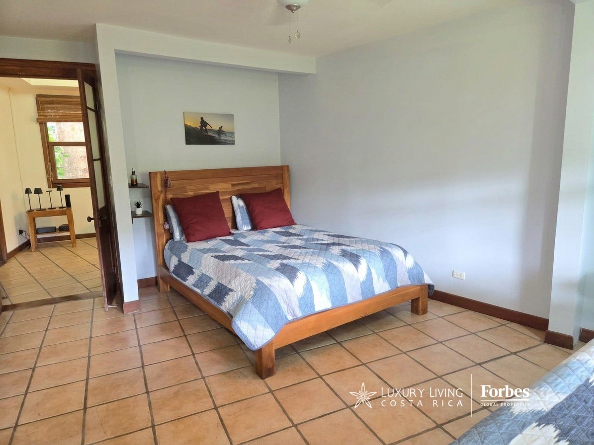 Bedroom with a wooden bed, blue-and-white quilt, burgundy pillows, and tiled flooring.