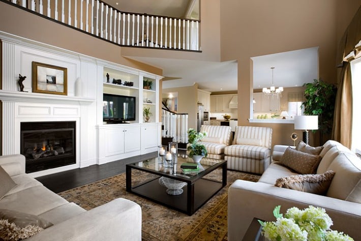 Staged living room with a white fireplace, built-in shelves, cream sofas, and an open kitchen.