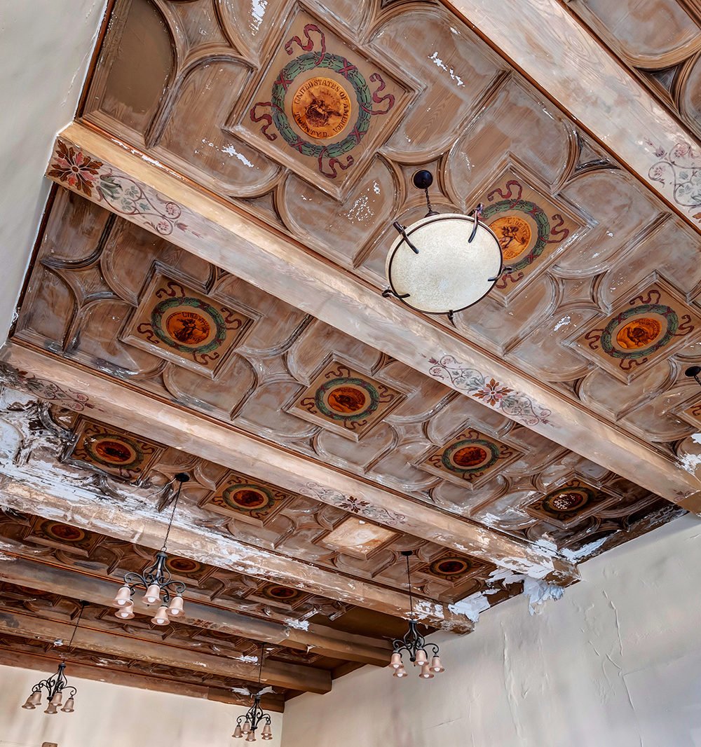 Ornate coffered ceiling with painted medallions, carved woodwork, and hanging chandeliers.