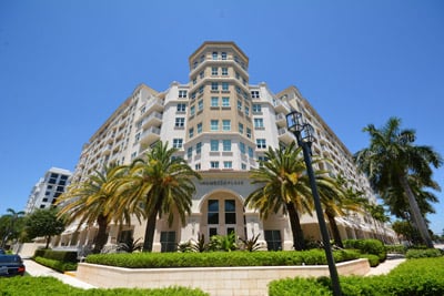 Luxury condominium exterior with a beige central tower, palm trees, and landscaped grounds.