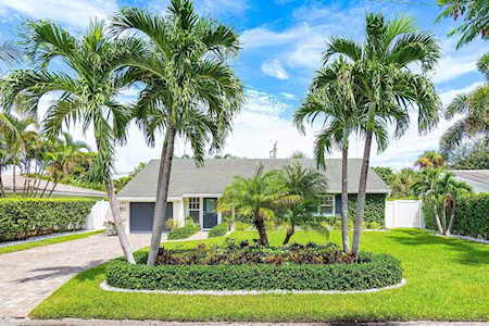 Single-story home framed by tall palms, with a landscaped front garden and curved driveway.