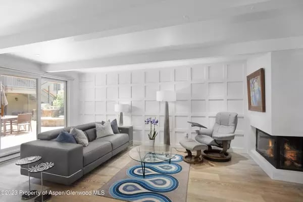 Living room with a gray sectional, blue patterned rug, and corner fireplace.