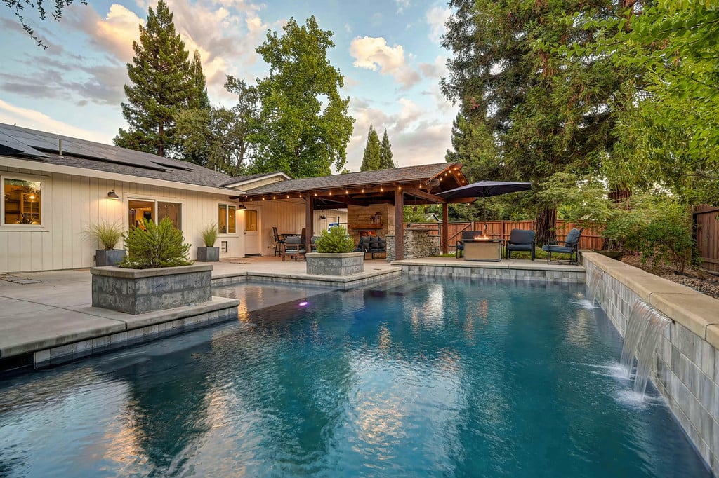 Backyard pool with a stone waterfall edge beside a covered patio and outdoor kitchen.