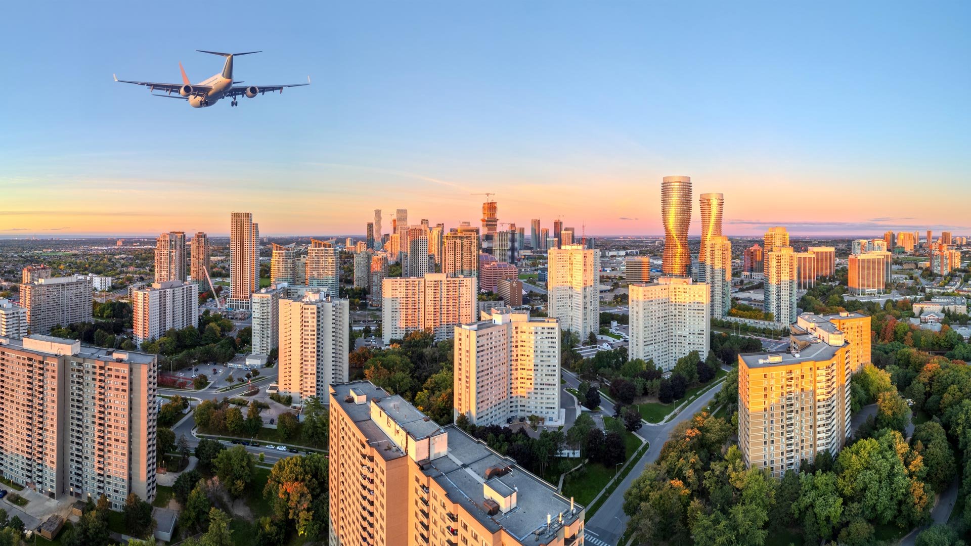 A stunning aerial golden hour photograph of the Mississauga skyline with a commercial airplane flying overhead, highlighting the city&rsquo;s connectivity and urban appeal for those moving to Mississauga