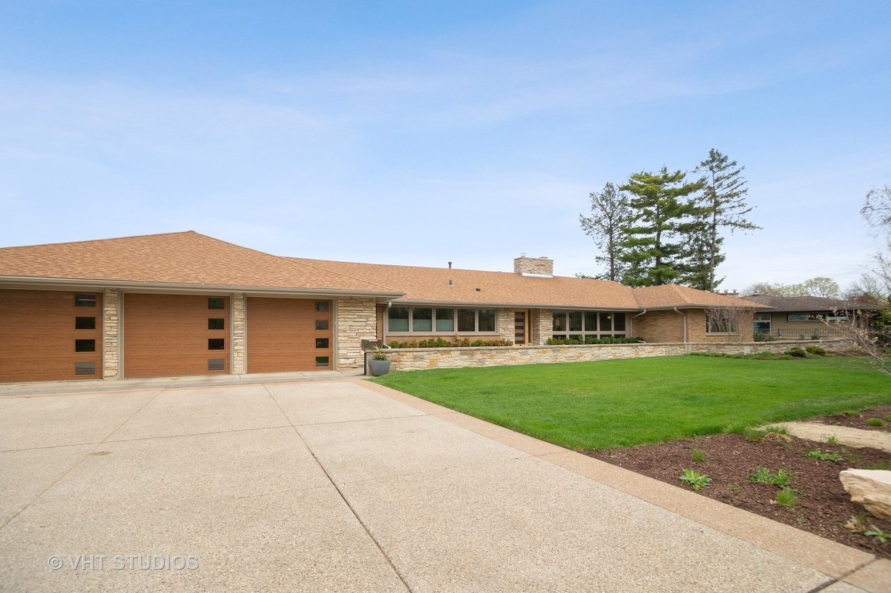 Single-story stone-and-brick home with three wooden garage doors and a broad driveway.