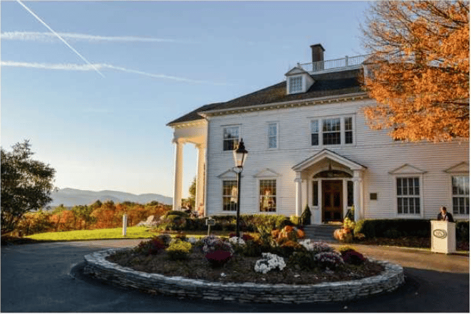 White resort building with a columned entrance, autumn foliage, and distant mountain views.