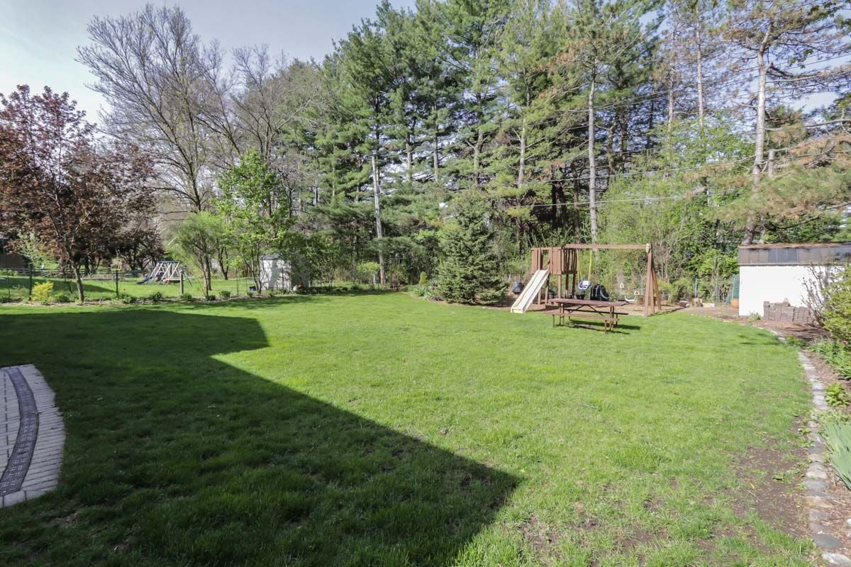 Spacious grassy backyard with a wooden playset, picnic table, mature trees, and a small shed.