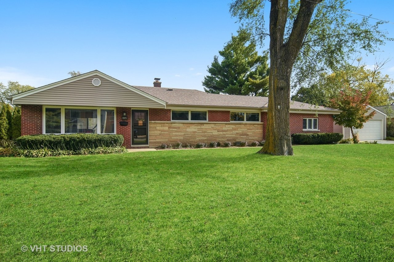 Ranch house with brick and stone facade, attached garage, and a large tree in the front lawn.
