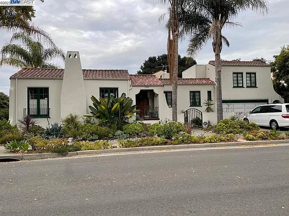 White stucco home with red tile roofs, landscaped garden, and palm trees.