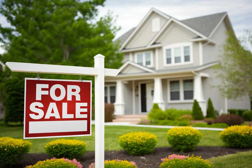 Gray two-story house with a prominent FOR SALE sign and landscaped front yard.