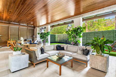 Covered patio with a wood-plank ceiling, sectional seating, and views of a fenced garden.