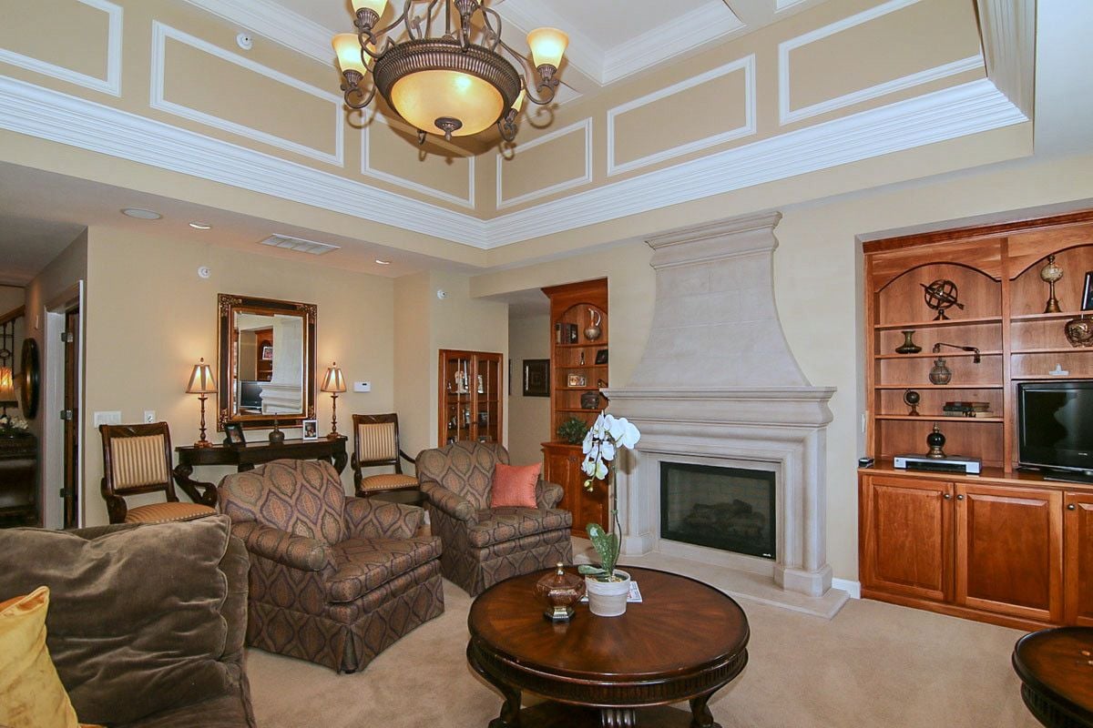 Penthouse living room with a stone fireplace, built-in wood shelving, and ornate chandelier.