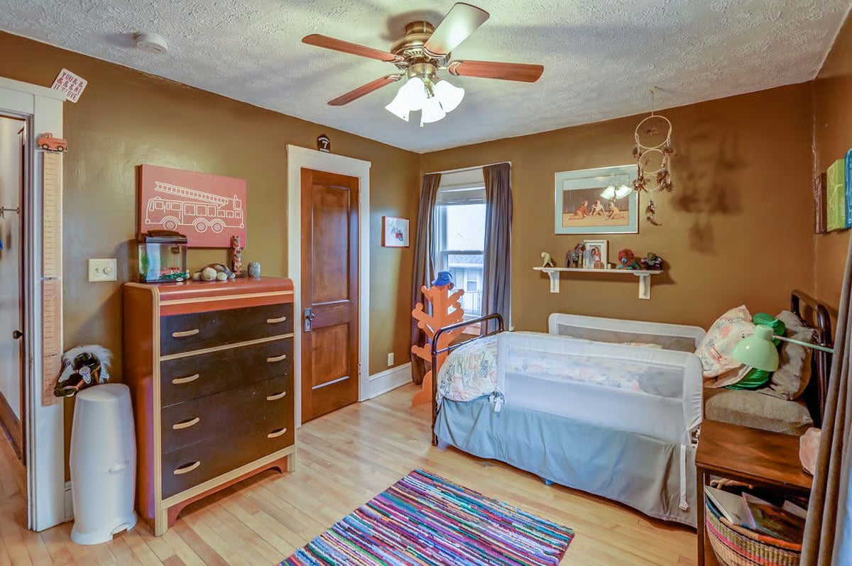 Child’s bedroom with two beds, a dresser, ceiling fan, and colorful striped rug.