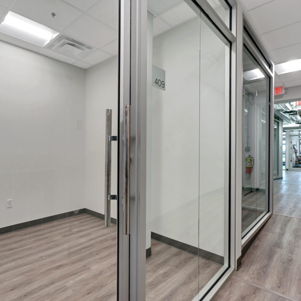 Vacant office suite with glass walls and a 409 sign, viewed from the hallway.