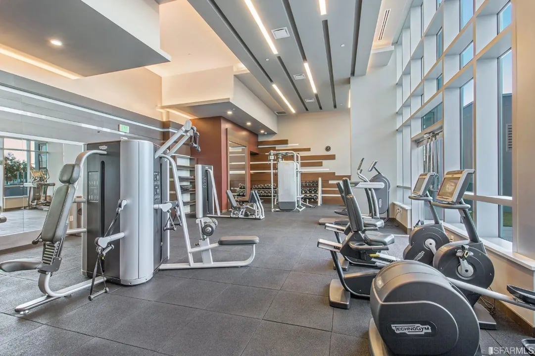 Arden Residences state-of-the-art fitness center with modern exercise equipment, cardio machines, weight training area, and large windows in Mission Bay